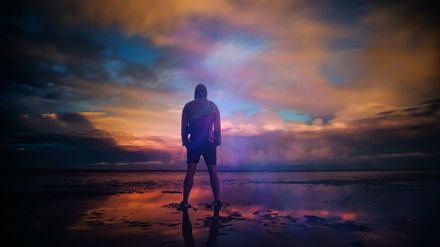 Un homme de dos se tient debout déterminé devant la mer au lever du soleil